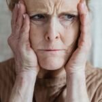 Older woman with hands near her face looking mentally fatigued, illustrating brain fog