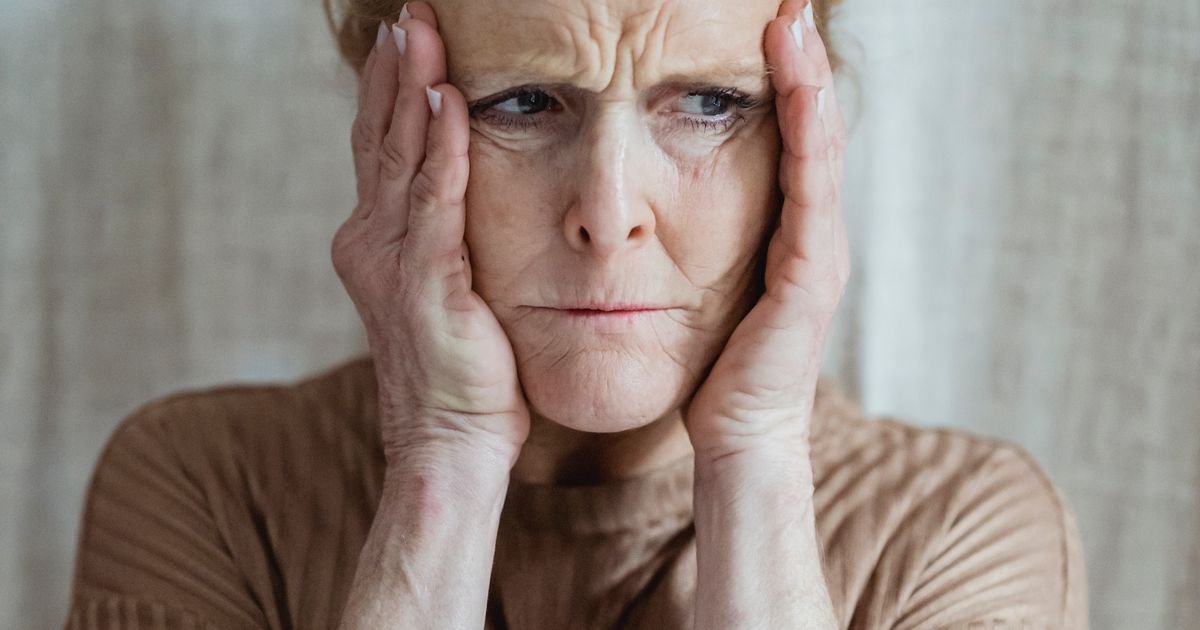 Older woman with hands near her face looking mentally fatigued, illustrating brain fog