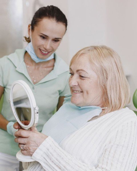 Senior woman smiling while checking her teeth in a mirror with a dentist