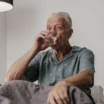 Senior man sitting up in bed at night drinking a glass of water