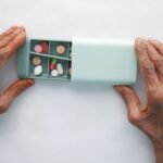 Elderly hands opening a weekly pill organizer containing several medications