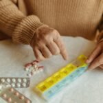 A senior adult's hands organizing daily medications into a weekly pill organizer on a table