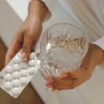 Hands holding a blister pack of pills and a glass of water at bedtime