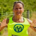Joyful senior woman in athletic gear celebrating outdoors after a run, hands raised in triumph