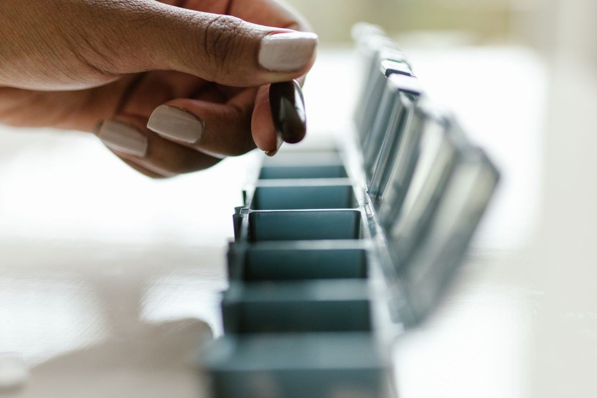 A hand holding a capsule near a colorful daily pill organizer, representing consistent daily supplement use