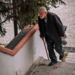 Elderly man using a cane while navigating stairs due to knee pain