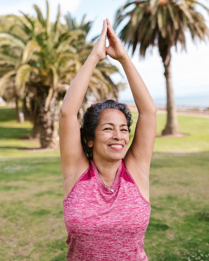 Senior woman smiling during a yoga stretch in a sunny palm-tree park