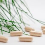 Natural herbal supplement capsules with green leaves on a white background