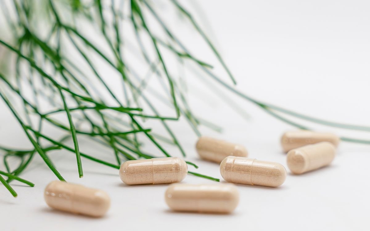 Natural herbal supplement capsules with green leaves on a white background