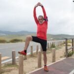 Elderly man stretching outdoors on a scenic path, demonstrating a hip flexor stretch