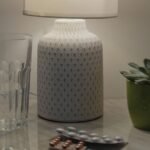 A cozy bedside nightstand at night with a lamp, a glass of water, a small succulent plant, and a blister pack of pills