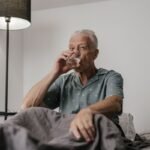 Senior man with gray hair drinking a glass of water in a bedroom setting