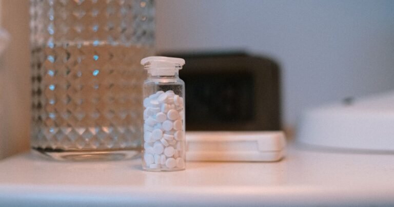 Close-up of a glass of water and a bottle of sleep medication on a bedside nightstand