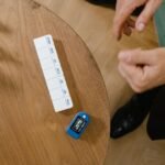 Overhead view of a senior man's hands near a weekly pill organizer and pulse oximeter on a wooden table