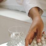 Hand reaching for a blister pack of tablets next to a glass of water on a bedside surface