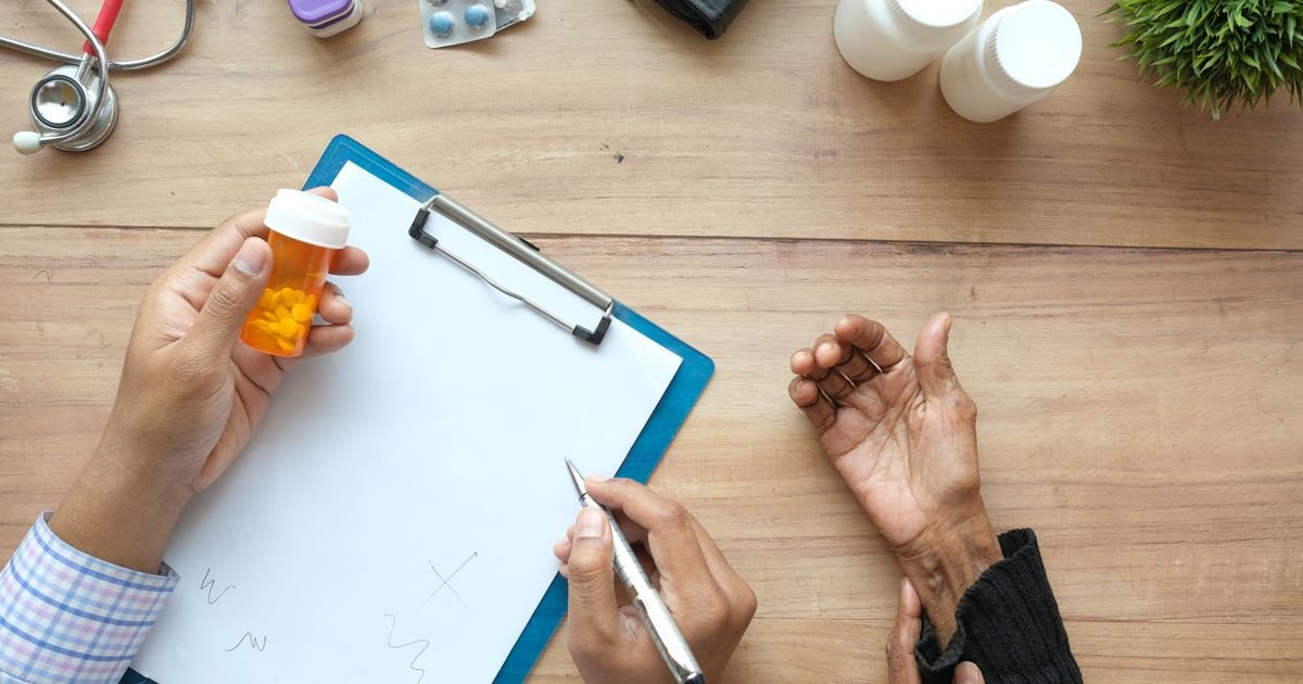Doctor reviewing a prescription with pill bottles and a clipboard, patient's hand resting on the table