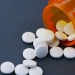 Close-up of white pills scattered from an orange prescription bottle on a gray surface