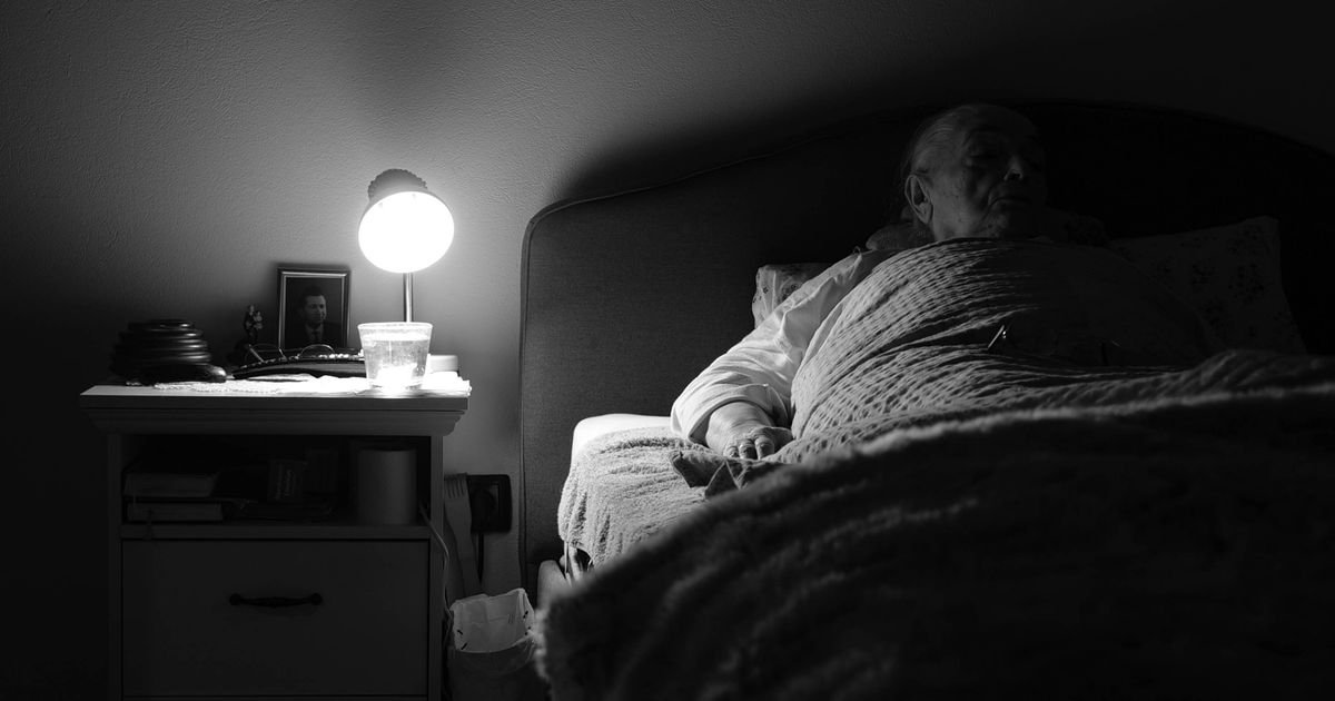 Elderly person resting in bed in a cozy, dimly lit bedroom