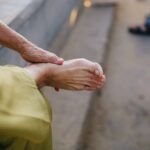 A weathered hand gently touching a bare foot, indicating foot pain