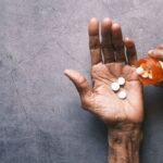 Elderly hand pouring ibuprofen tablets from a pill bottle