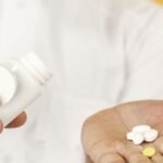 A doctor in a white coat pours tablets from a bottle into a patient's open hand