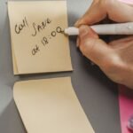 Close-up of a hand writing a reminder note on a sticky note