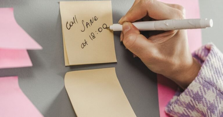 Close-up of a hand writing a reminder note on a sticky note