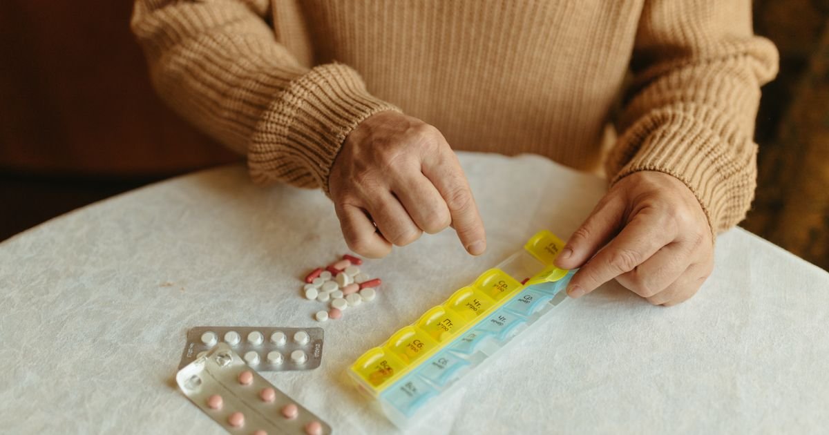 Senior adult organizing daily medications into a weekly pill organizer on a table.