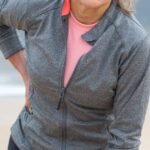 Senior woman holding her lower back outdoors, showing signs of back discomfort