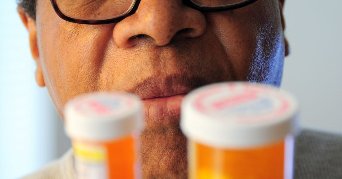 Senior man examining two prescription pill bottles indoors.
