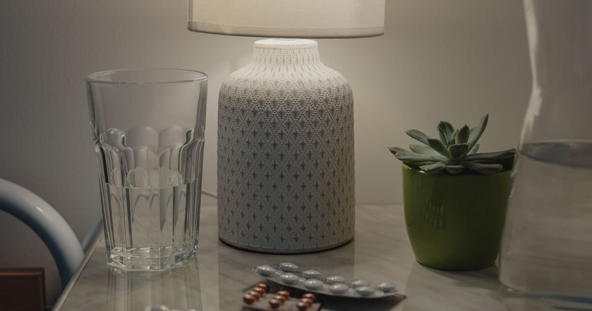 Nightstand with lamp, glass of water, and medication tablets in a cozy bedroom