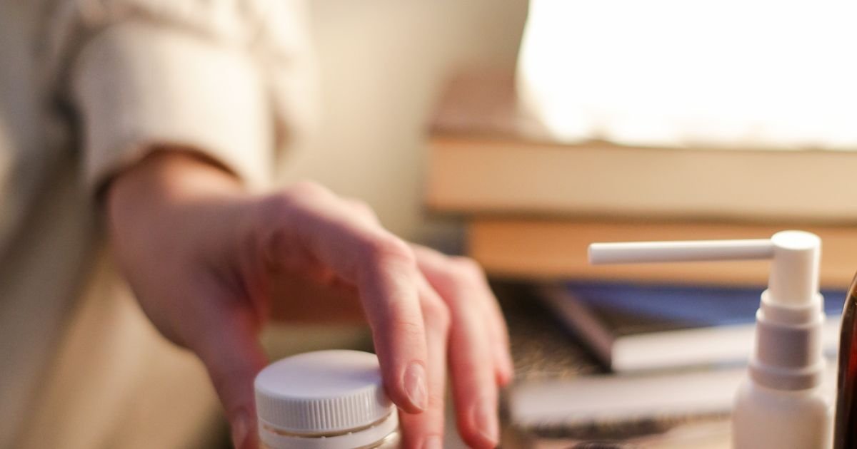 Close-up of a hand reaching for medicine pills on a nightstand